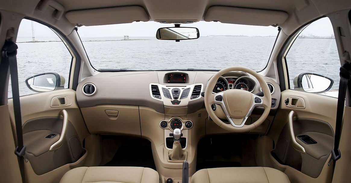 Tan car dashboard and steering wheel overlooking a calm body of water.