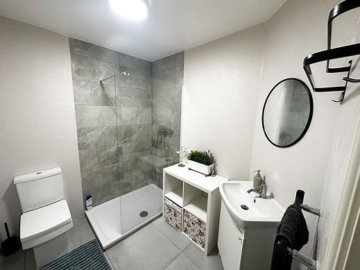 A modern bathroom with a walk in shower grey tiled walls white basin round mirror and toilet
