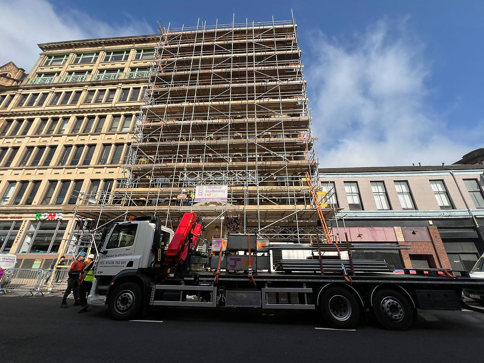 Scaffolding erected around a historic dark brick building in Glasgow with construction workers and a lorry