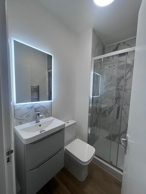 Contemporary bathroom with LED illuminated mirror white vanity unit and glass shower cubicle
