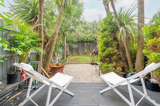 Two white deck chairs on a grey wooden decking overlooking a gravelled garden area