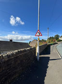 A road curves uphill next to a stone wall and houses.
