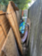 Before garden clearance with overgrown grass, garden waste, broken furniture and unwanted debris.