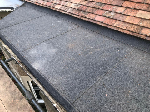 Newly resurfaced black flat roof section next to red clay tiles