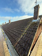 A man inspects roof insulation in an attic using a handheld device while wearing protective gear.