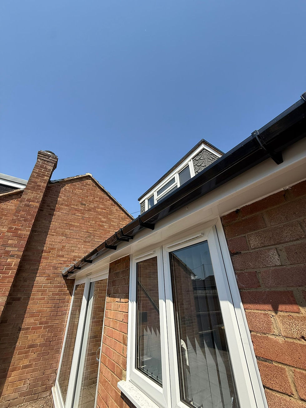 A white rain gutter and downspout attached to the soffit of a yellow house against a clear blue sky