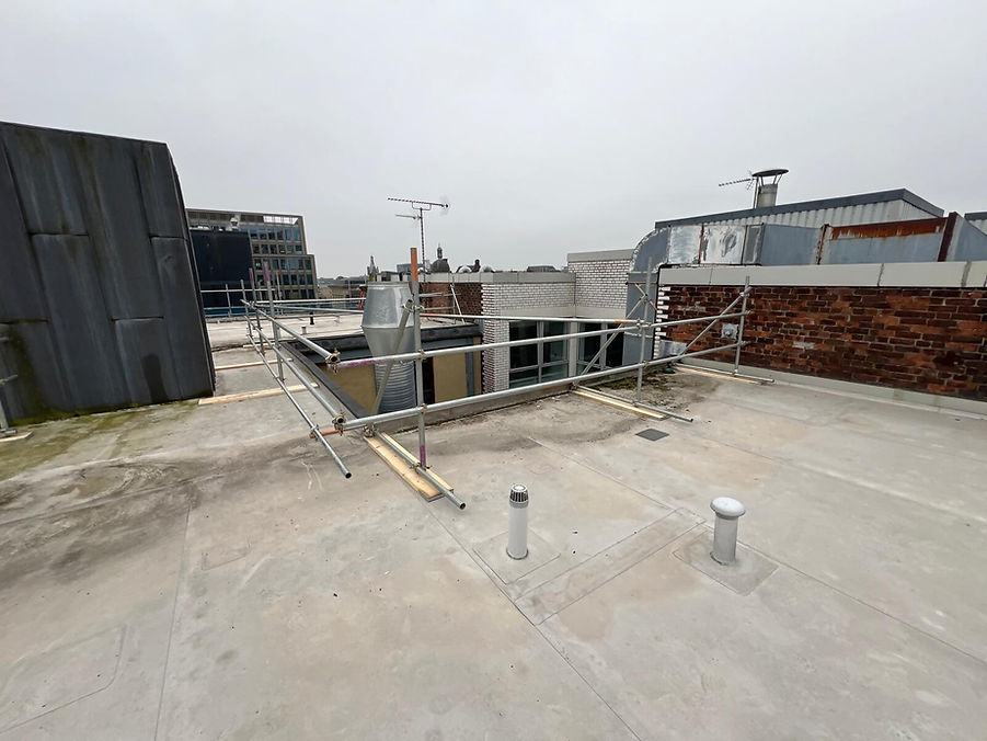 Flat rooftop under construction with scaffolding and brick parapet walls nearby