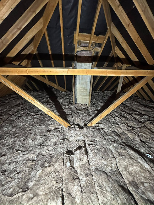 Thick layers of dark mineral wool insulation rolled beneath attic framework joists