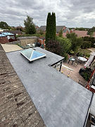 A flat roof with black waterproof membrane and small roller tool next to a drainage hole.