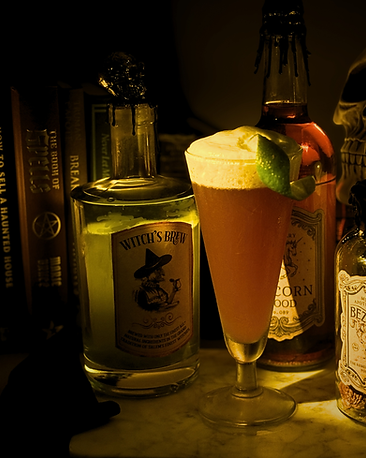 Bourbon cocktail with foam and lime garnish, books in background.