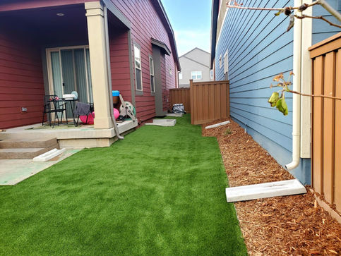 Narrow yard with artificial turf, patio, and wood chips