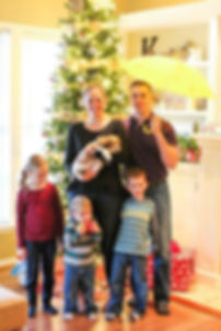 Family of five stands in front of the Christmas tree holding a new puppy and a yellow umbrella