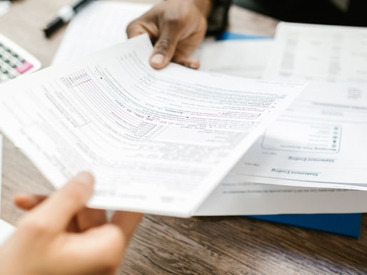 Hands exchange documents over a wooden desk with a calculator nearby, suggesting a business or financial setting. Representing a Notice to Owner Florida.