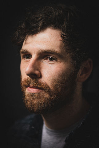 Composer James Creed in a moody, low-key portrait with dramatic lighting emphasizing his thoughtful expression.