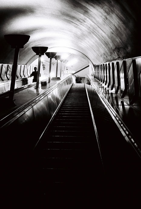 Black-and-white view looking up a long London Underground escalator in a curved tunnel.