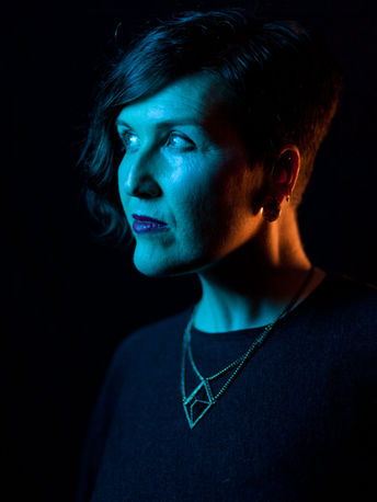 Gel-lit profile portrait of a woman looking left, blue key light with warm rim light on black background.