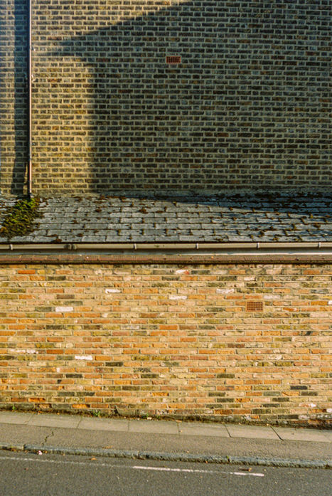 Stacked brick walls with slate roof and deep shadow line forming a bold horizontal composition on a London street.