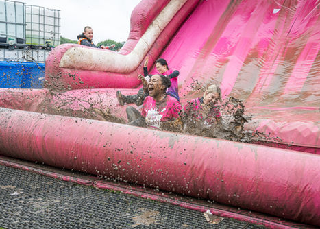 Race for Life participants laughing and splashing through mud on a large pink inflatable obstacle.