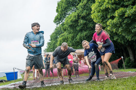 Four muddy Race for Life participants laughing together beside a cargo net obstacle.