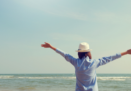 Woman standing by the ocean with arms raised, symbolizing freedom, peace, and taking back control of life.