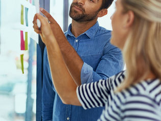 Dois colaboradores a planear projetos com post-its coloridos numa parede de vidro