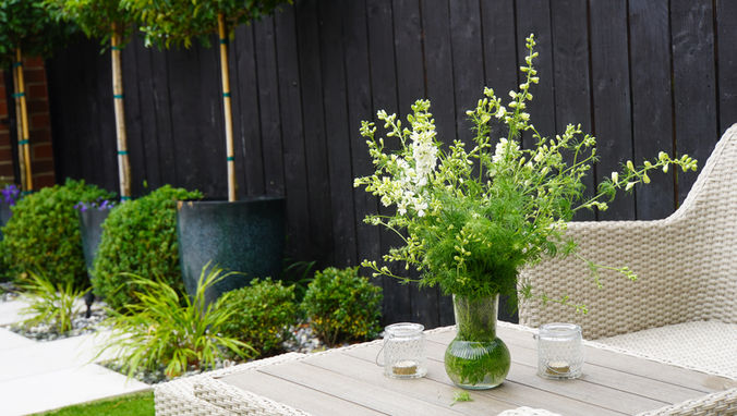 A beautiful punch of freshly picked flowers sits on the table of a cream garden sofa set, within a high contrast contemporary elegant garden 