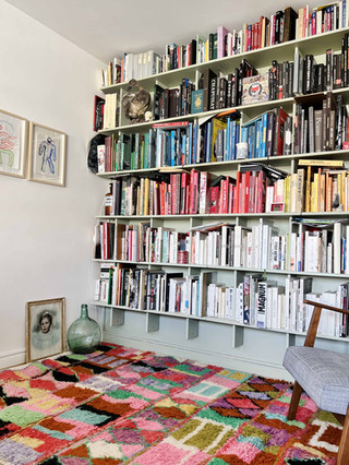 Tapis Boujaad coloré dans bibliothèque avec livres d'art, collection de livres photos, cadres anciens, dame jeanne, fauteuil chiné et oeuvres d'art
