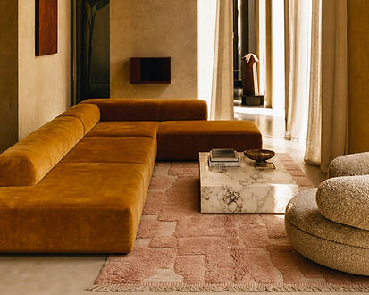 Ein puderrosa Berberteppich, ein senffarbenes Sofa und ein Marmortisch in einem Interieur im Bohème-Stil