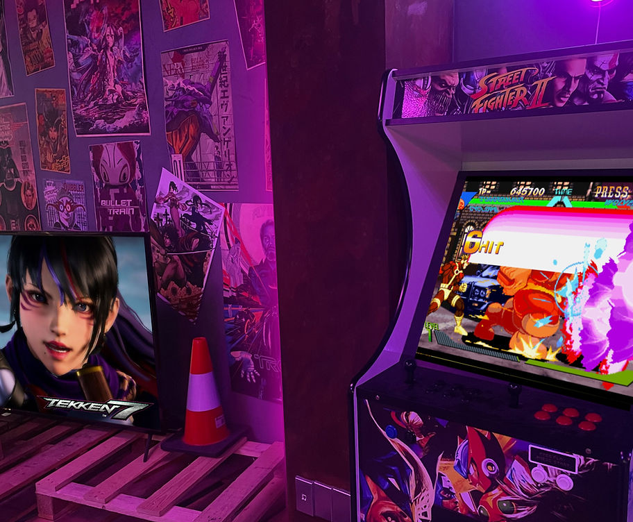 The Fox's Mark cyberpunk studio waiting room with arcade machine and TV setup like a tokyo back alley with palettes and rode cones and movie posters on the concrete wall. Tekken 7 and marvel vs capcom on the screens