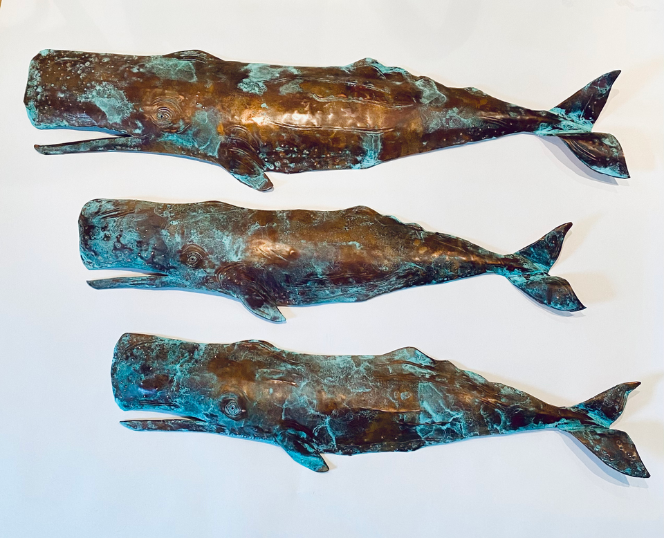 Three copper sperm whale sculptures with a turquoise and copper patina finish.