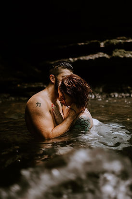 man and woman in the water with a cliff behind them caressing each other