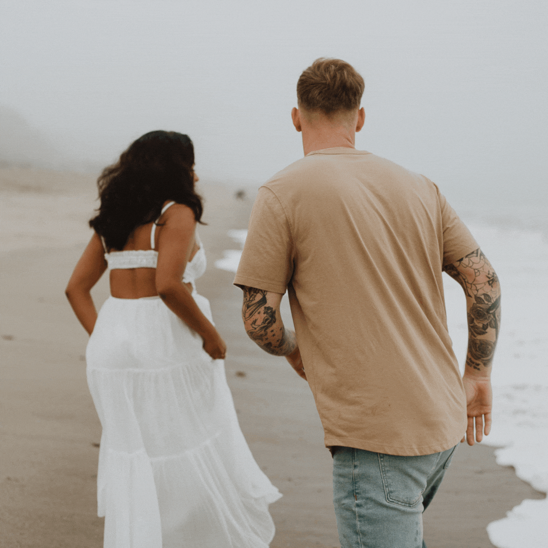 man and woman holding hands running along the beach in the fog