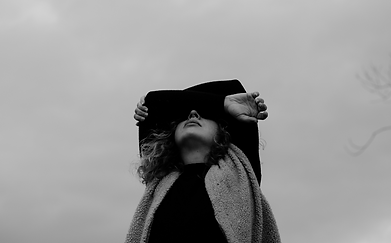 A black and white image of a woman looking up, folding her arms over her face