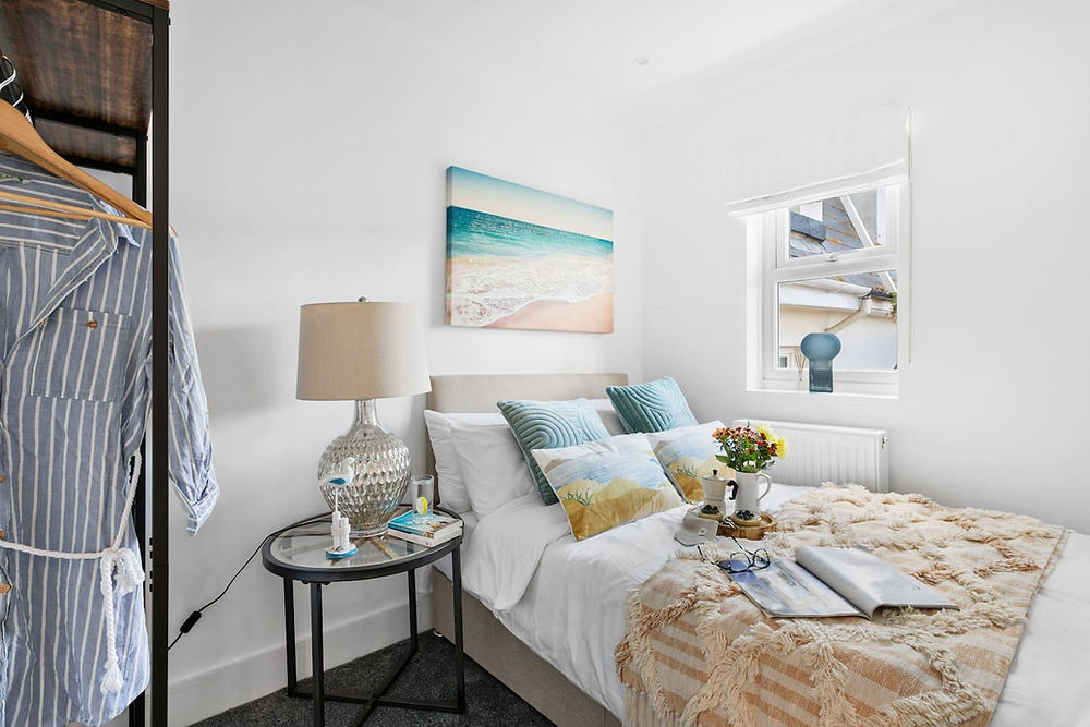 Bright bedroom with a bed, nightstand, lamp, and ocean painting.
