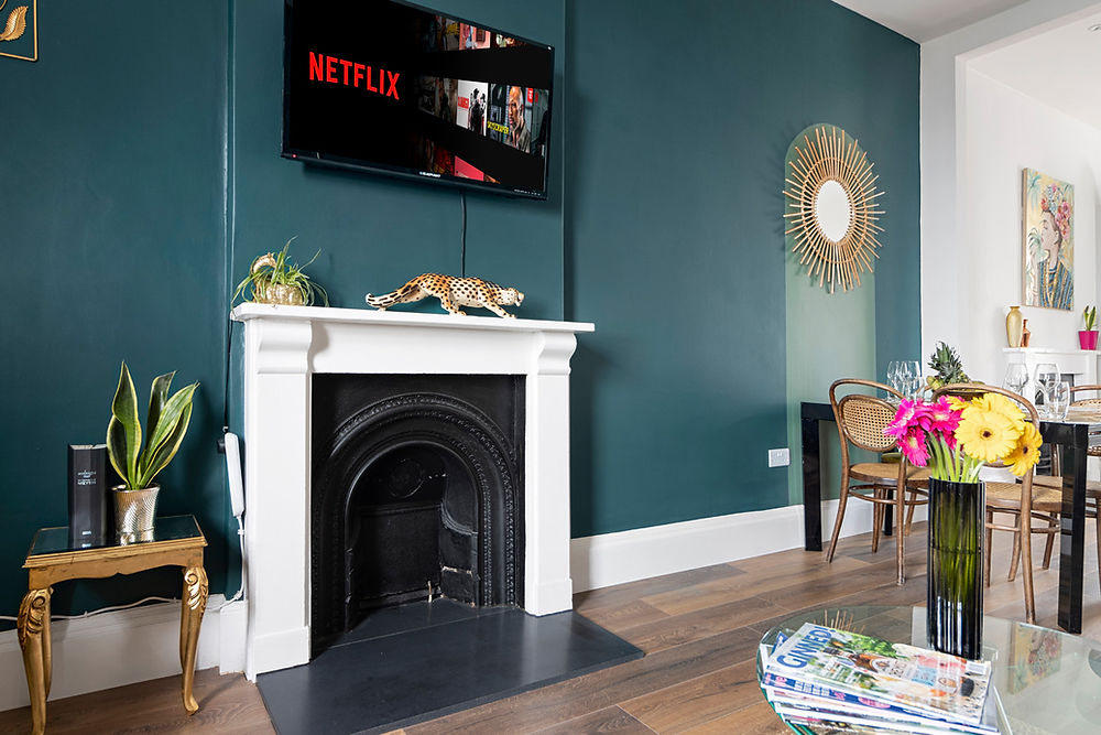 Living room with teal wall, fireplace, TV showing Netflix, and flowers