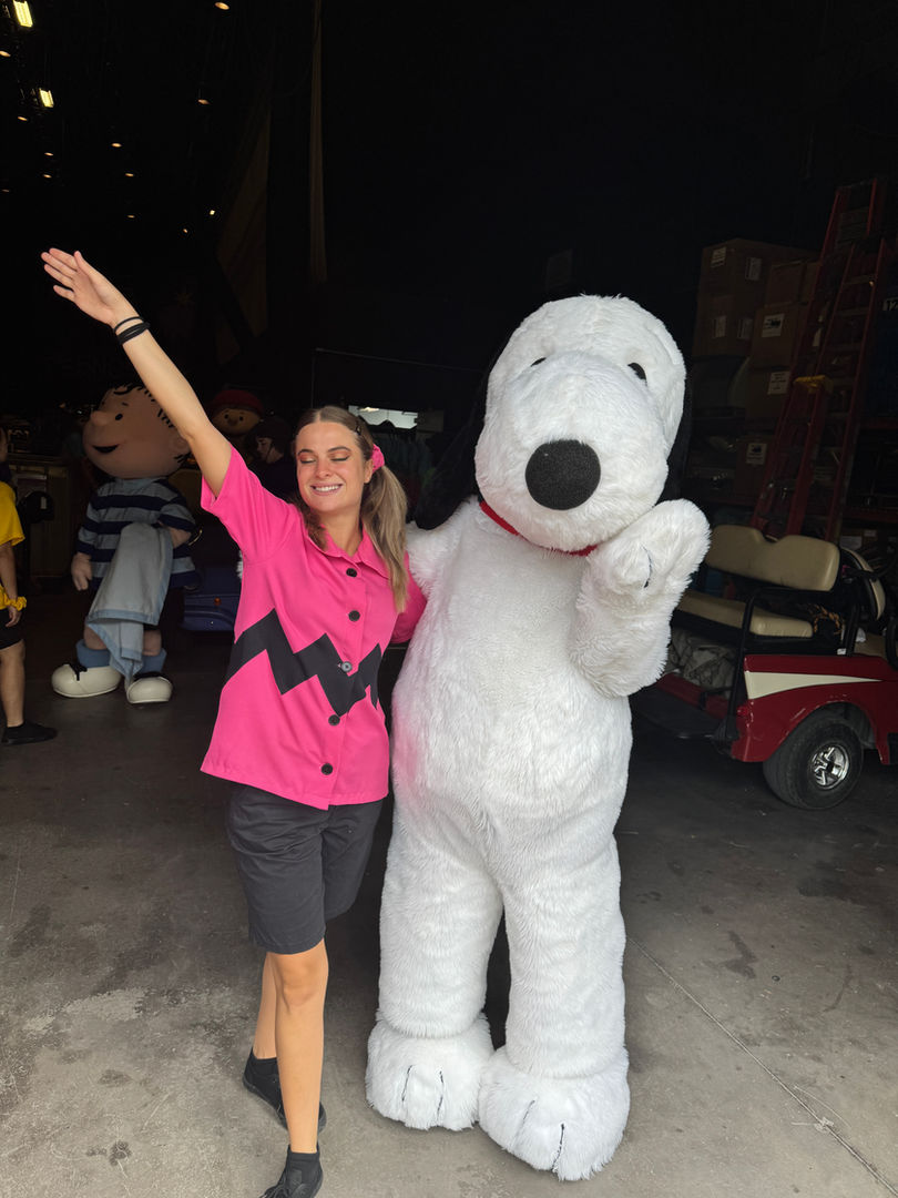 Smiling woman in pink Charlie Brown shirt poses with Snoopy mascot.