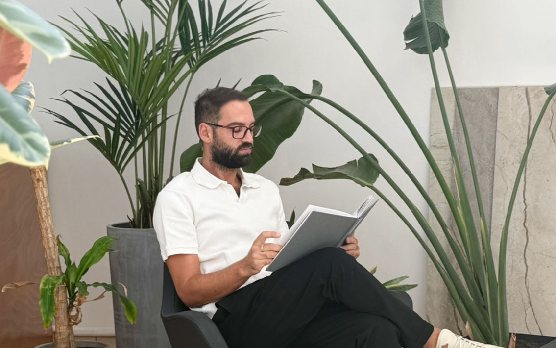 Kyriakos sitting reading a book by foliage and marble