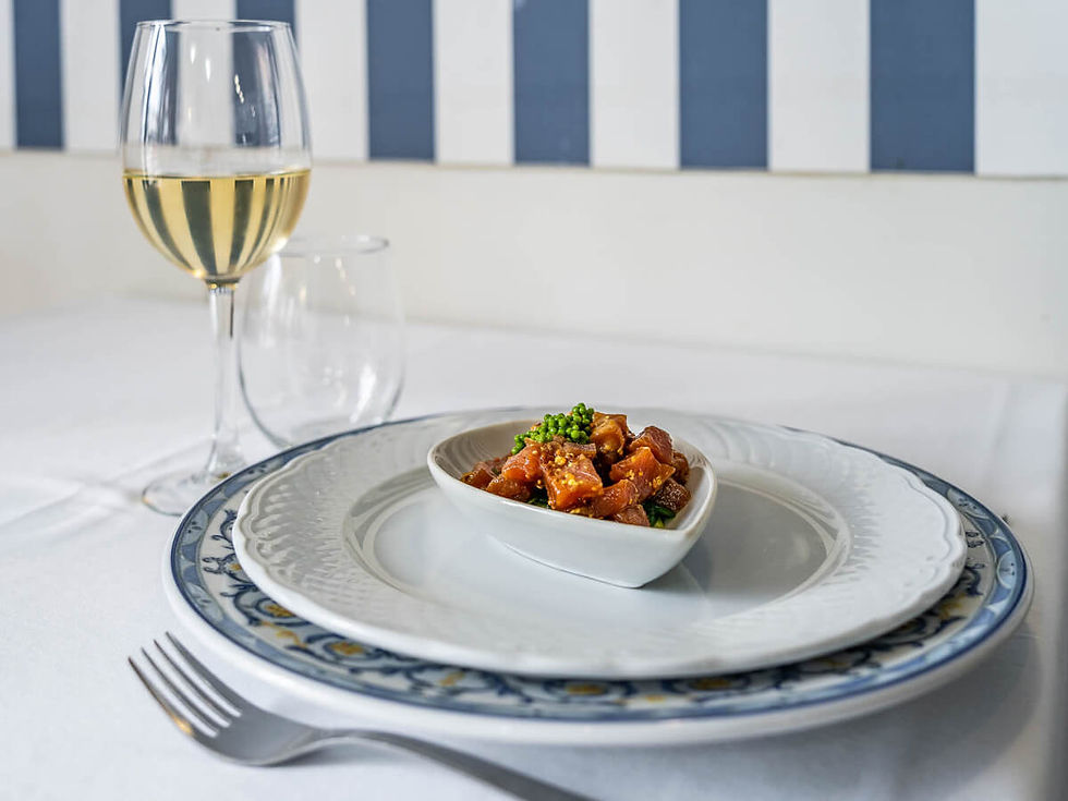 Table setting with wine, a small dish with diced food on a patterned plate, fork, striped blue and white background, elegant dining mood.