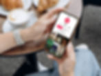 Person holding a phone showing an Airbnb TikTok profile with croissants and coffee on a table. Casual setting, relaxed mood.