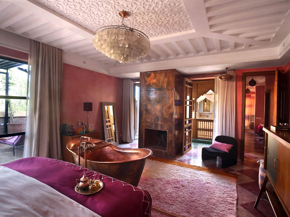 Luxurious room with a copper bathtub, plush rugs, and pink walls. A chandelier hangs from a decorative ceiling. Cozy and elegant ambiance.