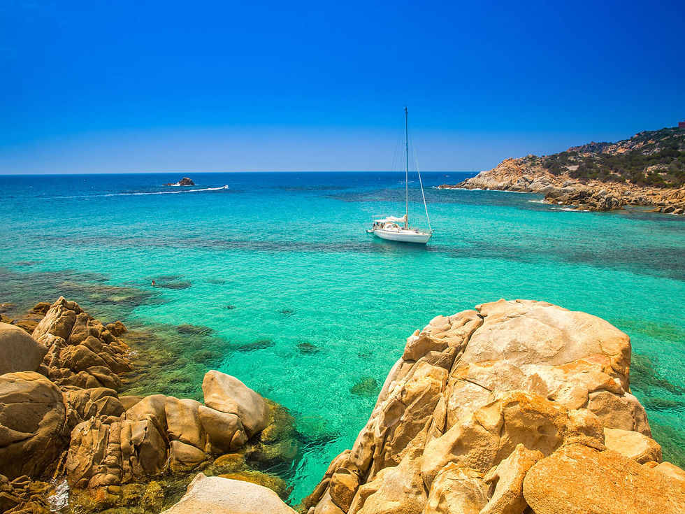 Sailboat on clear turquoise water near rocky shore under a vibrant blue sky, creating a tranquil and picturesque coastal scene.
