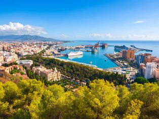 Panoramic coastal city harbor with cruise ships, blue sea, mountains, and green trees under a clear sky. Header image related to the blog post "Our Pick Of The Best Hotels in Málaga for 2026"