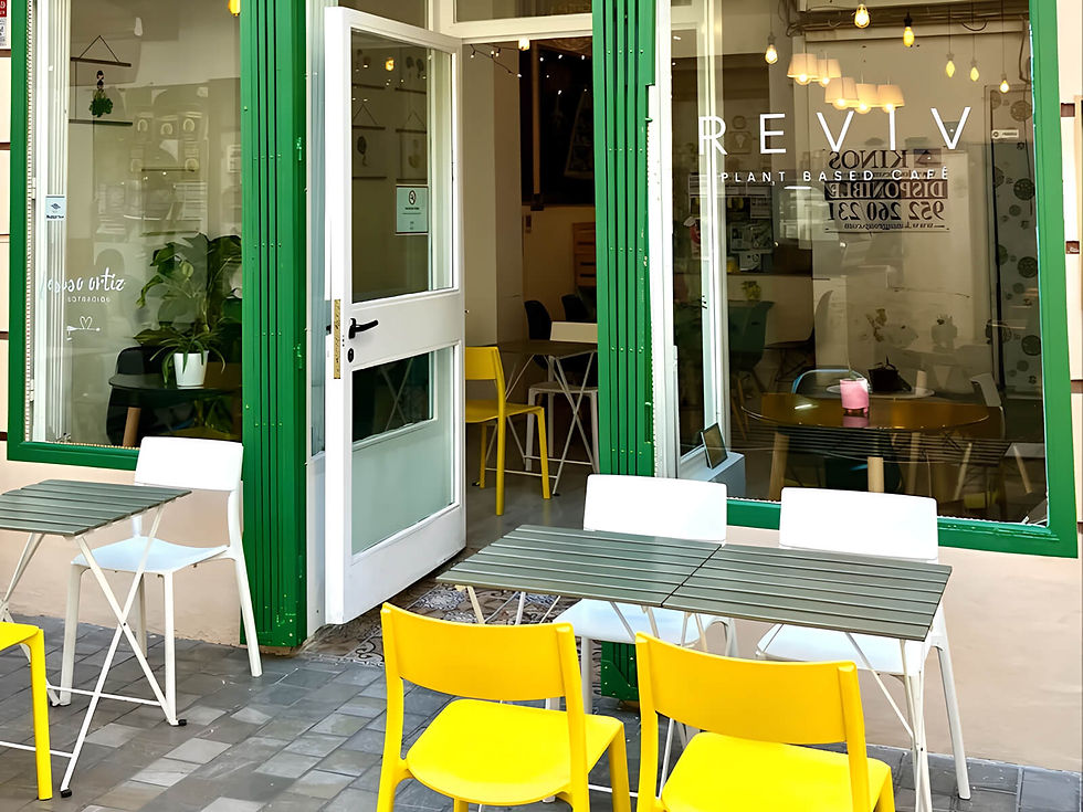 Exterior of REVIV plant-based cafe with open white door, green trim, and bright yellow chairs on a sunny patio.