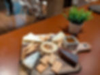 Cheese platter with crackers, breadsticks, and a sauce dip on a wooden board. A potted plant nearby on a brown table in a cozy room.