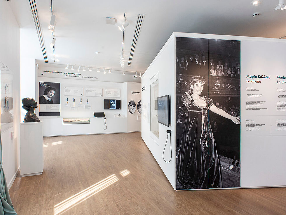 Gallery room with a black-and-white wall photo of a woman performing, accompanied by text. Bust sculpture and information panels displayed.