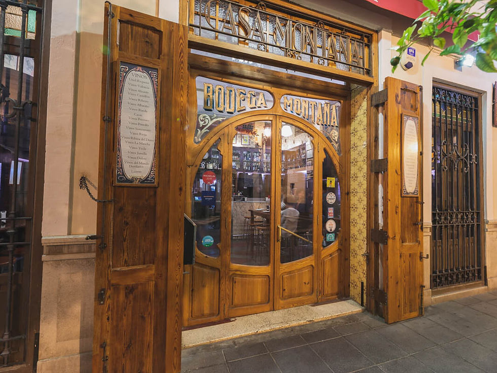 Rustic wooden entrance of Bodega Montaña, with decorative glass and wine list. Warm lights inside, creating a cozy, inviting atmosphere.