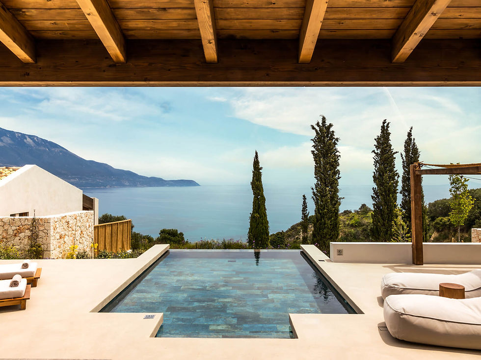 Luxurious poolside scene with loungers, overlooking a serene sea and mountains. Blue sky, tall cypress trees, and rustic stone walls enhance tranquility.