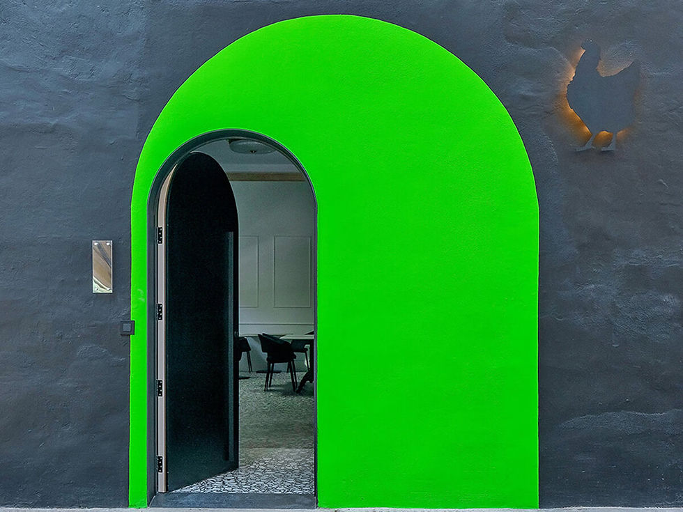 A vibrant green archway on a dark wall, partially open to a modern interior with chairs. A silhouette of a chicken is illuminated on the wall.