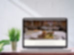 Hands type on a laptop showing a gourmet dish on screen. The setting is a wooden table, creating a cozy, focused atmosphere.