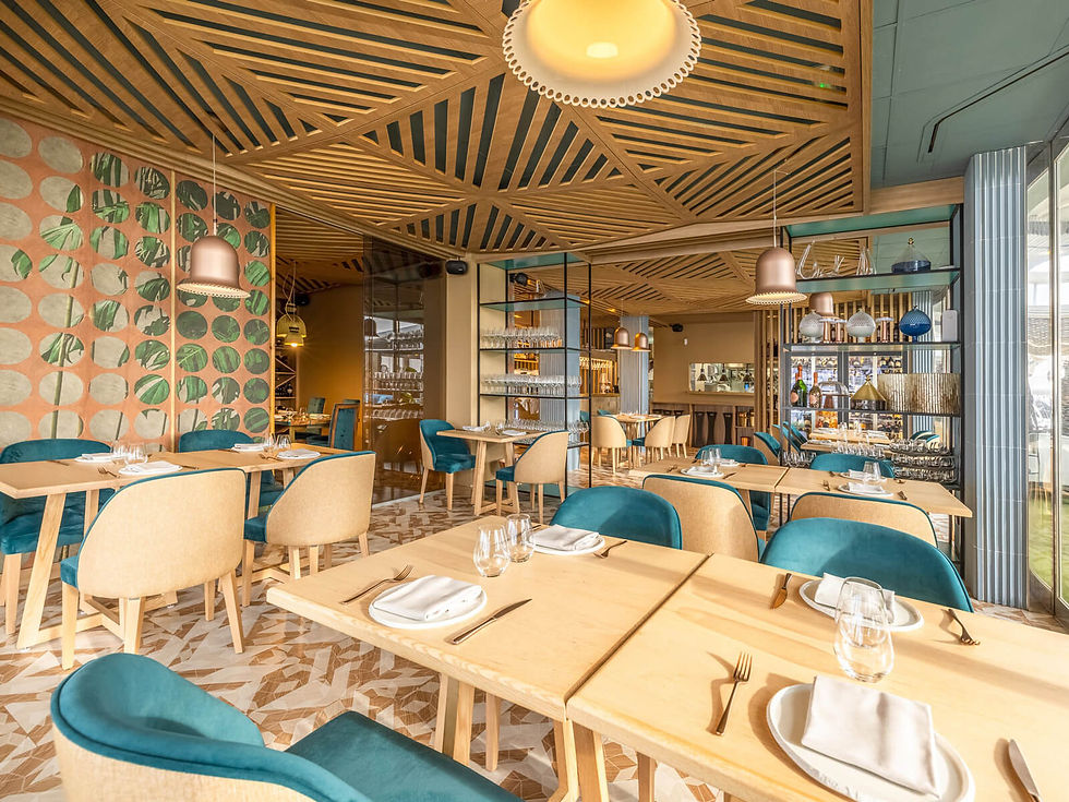 Modern restaurant interior with wooden tables set with napkins and glasses. Teal and beige chairs, geometric ceiling, leafy patterned wall.